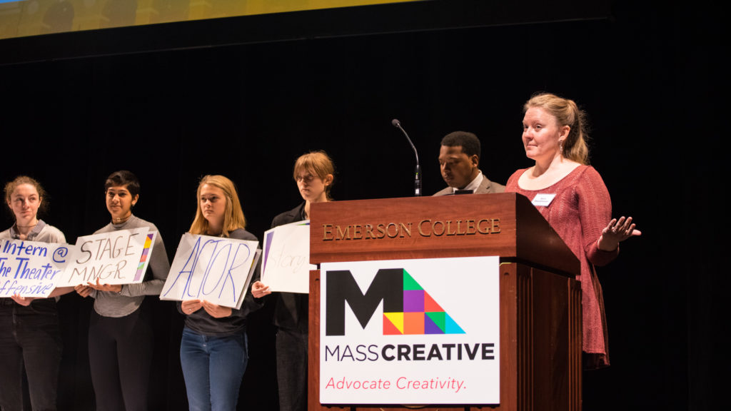 Sara Stackhouse, theater chair at the Boston Conservatory at the Berklee College of Music, speaks about her middle school chorus experience as young art students silently hold posters telling their personal stories about how the arts impacted them too. / Photo by Alex Melagrano