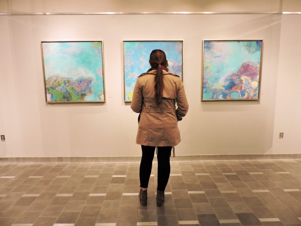 A visitor looks at paintings by Mary Hughes. / Photo by Ashley Wong