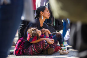 A woman and child sit on the pavement at Park Street Station while listening to speakers at the Rally for Indigenous Peoples Day on October 6. 