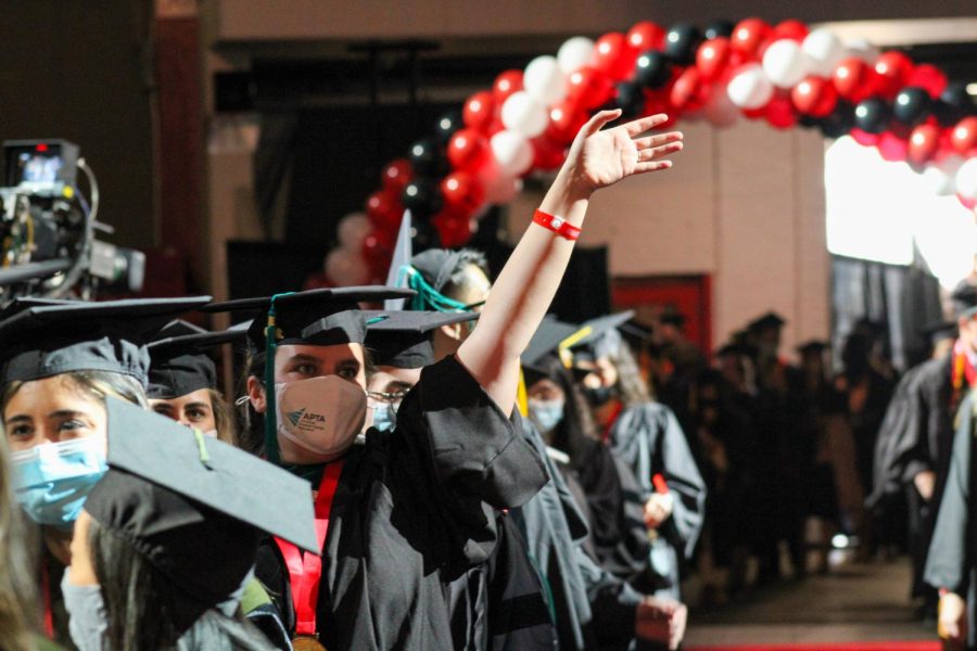 A graduate waves at the crowd while they process into Matthews Arena.