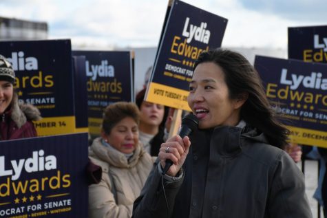 Michelle Wu, an Asian American woman, speaks to a crowd. Behind her, people hold signs supporting Lydia Edwards senate campaign.