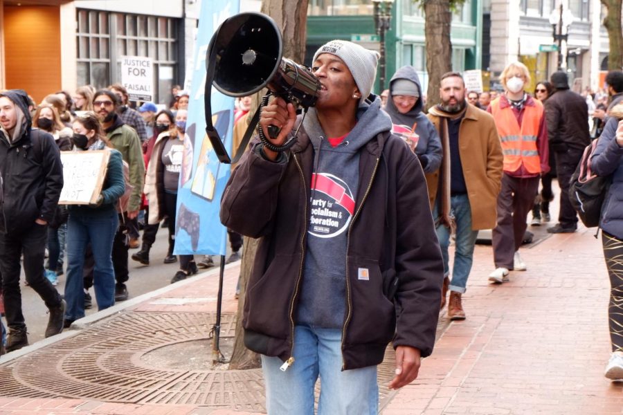 An organizer from the Party for Socialism and Liberation, Boston, speaks into a megaphone as they march down the street during Saturdays march. Protestors walked through downtown Boston, chanting phrases including“If we don’t get no justice, then they don’t get no peace!”