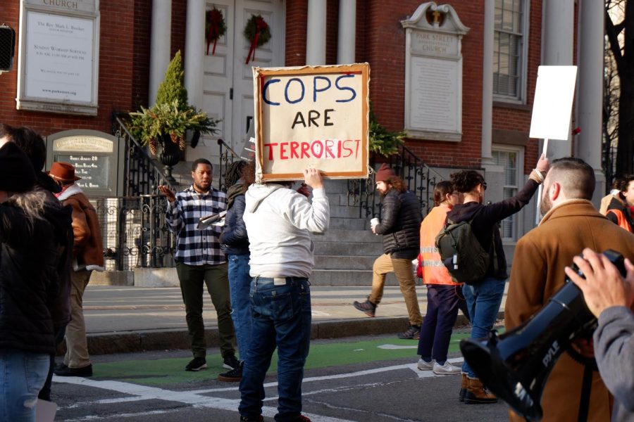 A protester holds a sign saying “Cops Are Terrorist” in front of Park Street Church during the protest Saturday afternoon. Alongside signs provided by the Party for Socialism and Liberation, many protestors handmade their own signs to bring to the march.