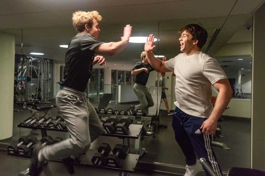 Students high-five after a workout in the International Village gym. Whether in a traditional gym or a dorm room, studies have found weight training increased mood and mental clarity.