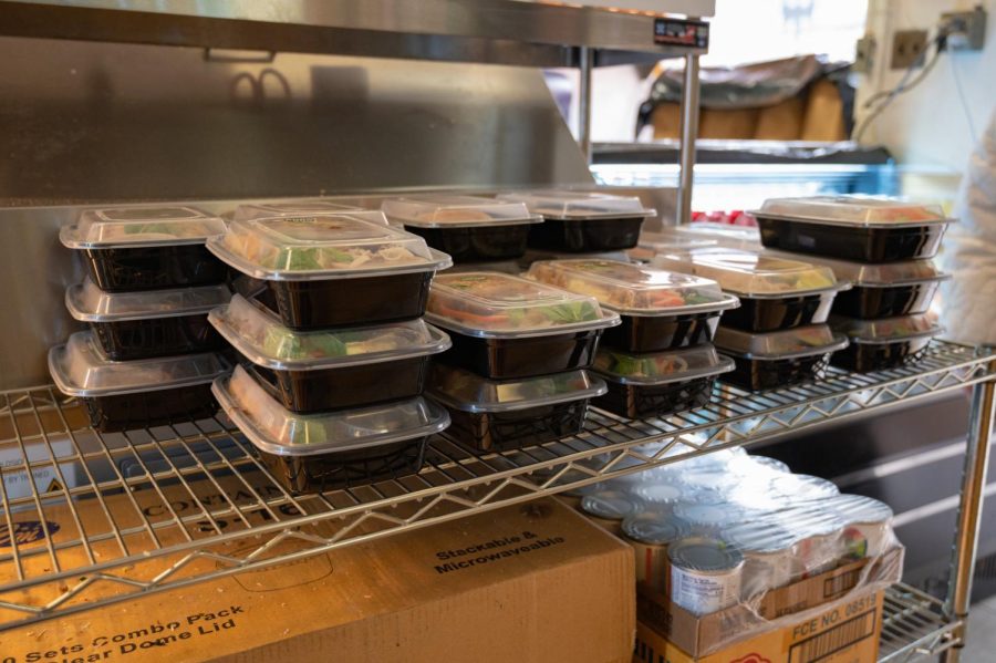 Stacks of meals sit on top of a wire shelf in the middle of the store. These meals, which include pork and chicken dishes, are pre-packaged and sold in convenient grab-and-go containers.