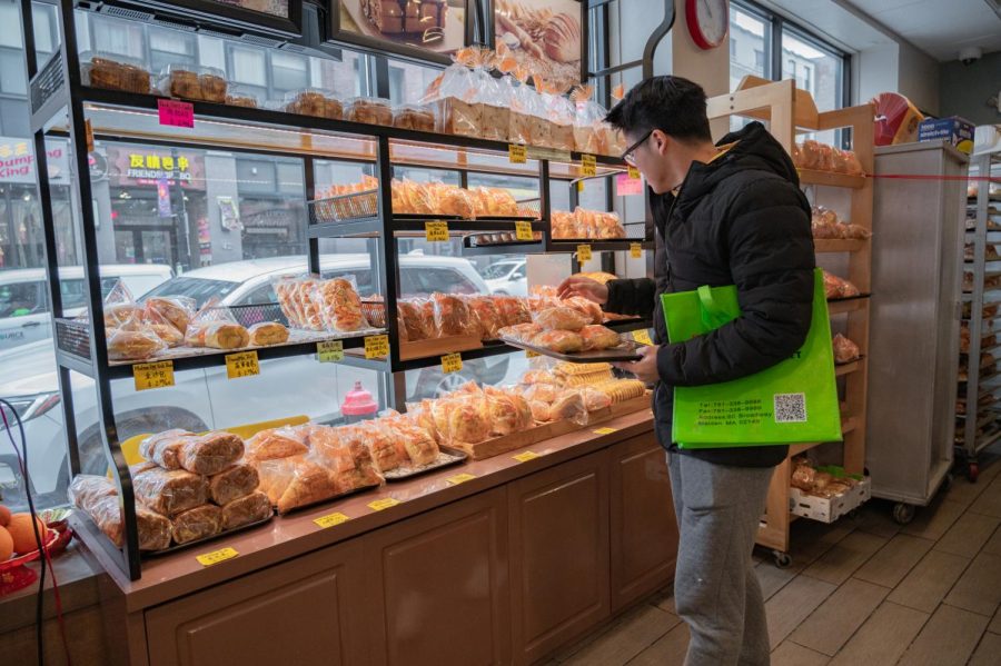 A customer reaches for a variety of buns at Corner Café Bakery. The store placed all of their bread products on a set of shelves to the left of the entrance.