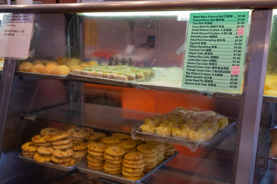 A list of prices is displayed in front of numerous trays of baked goods. Many customers have returned to Ho Yuen Bakery for their affordable and delicious offerings.