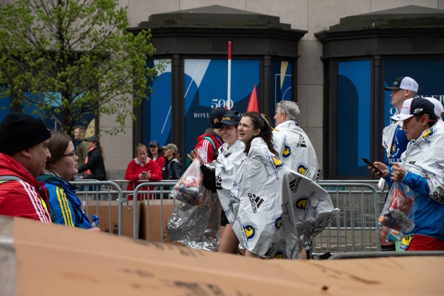 Wrapped in branded foil blankets, participants laugh in relief and joy after successfully finishing the marathon. Foil blankets were used to prevent excessive heat loss following high exertion by reflecting and trapping body heat.