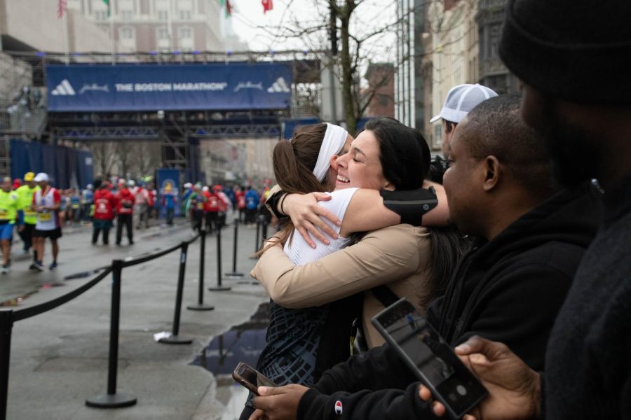 A runner embraces a loved one after crossing the finish line, seen in the background. The finish line was staffed with medical volunteers and people guiding participants to where they were receiving medals, blankets and greeting their friends and families.