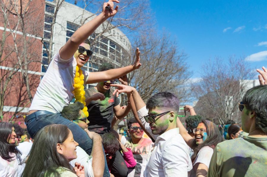 An attendee smiles while sitting on a friends shoulders during the Holi celebration.