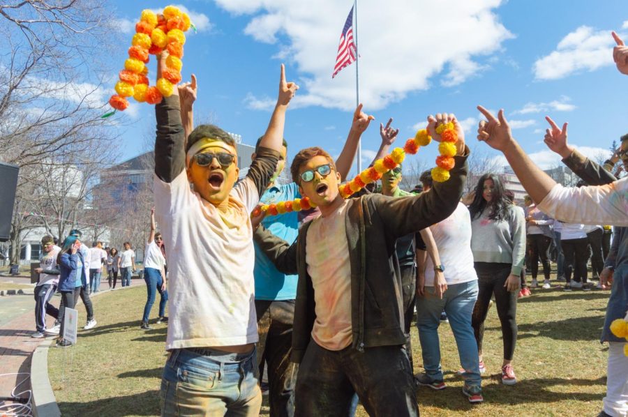 Two attendees pose for a photo while holding up orange and yellow festival flowers.
