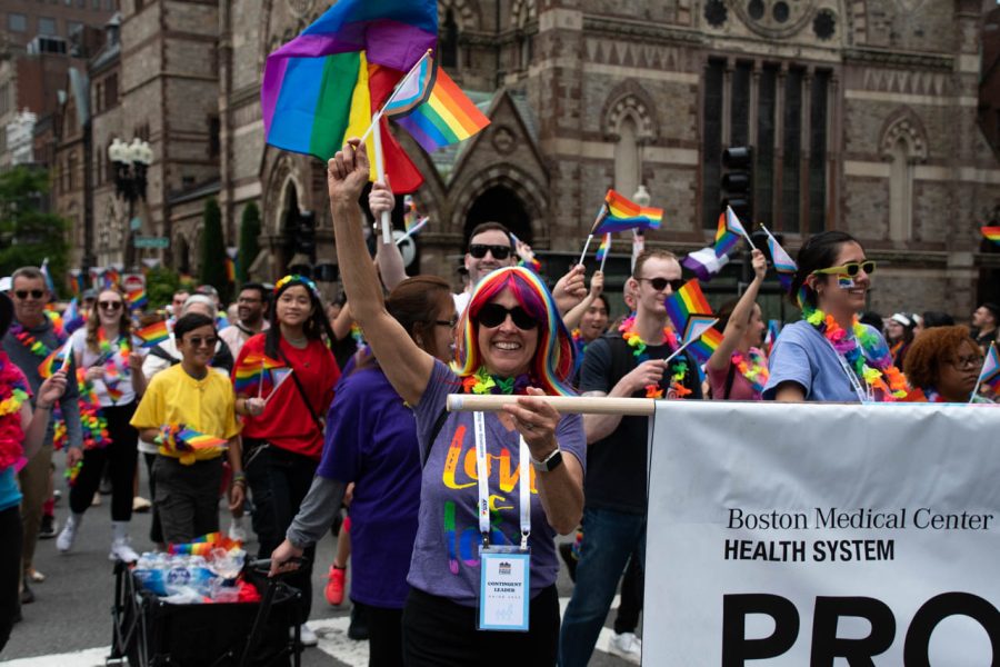 A woman smiles while holding a progress pride flag and the Boston Medical Center “Proud to Be” banner. The Boston Medical Center’s GenderCare Center provides gender-affirming care and other services to the community.