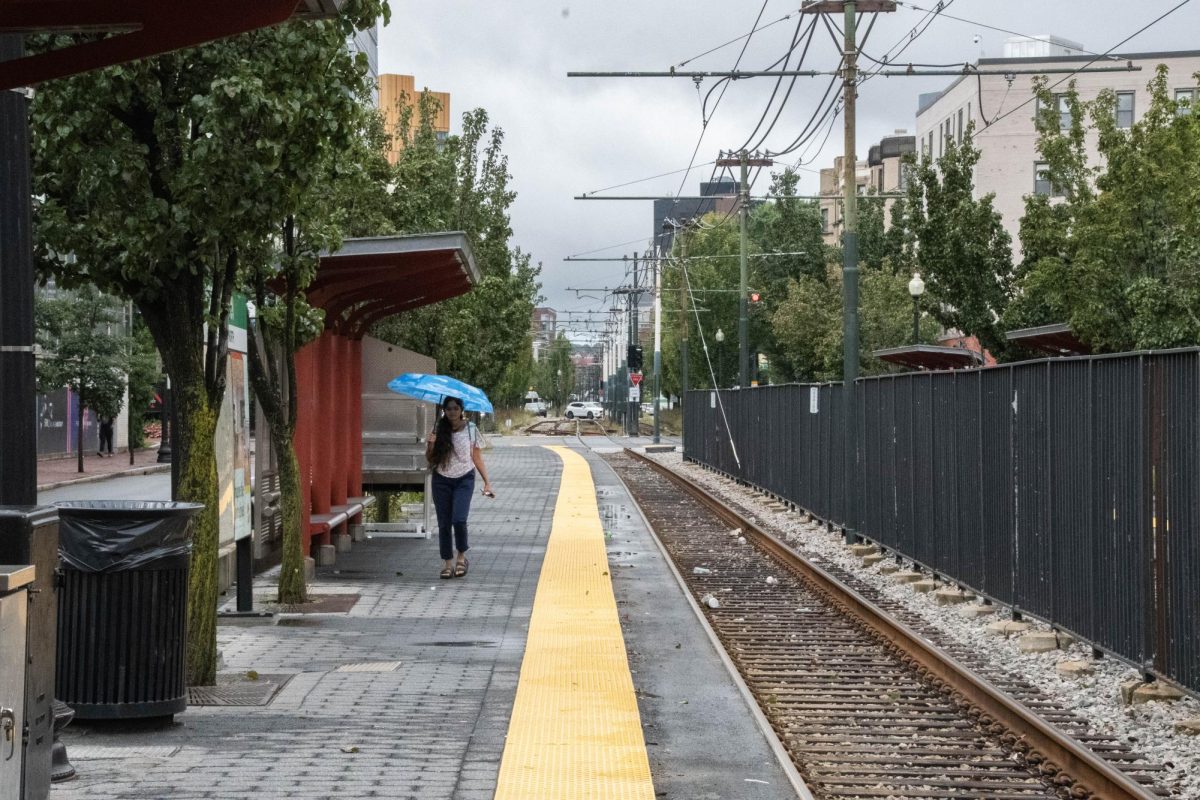 A woman holding a blue umbrella walks along the Northeastern T stop. Precipitation from June to mid-August in the Boston area was 17.72 inches, up from 4.42 inches in 2022.