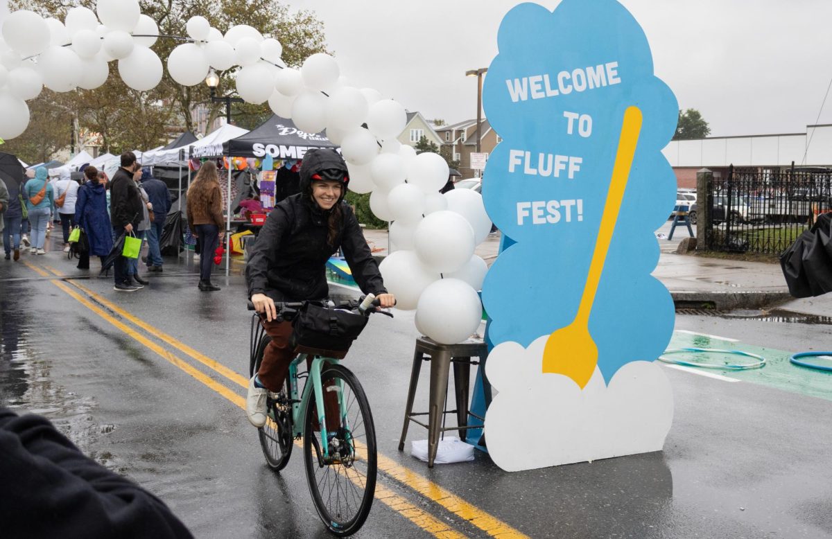 A biker goes under a white balloon arch and smiles for a photo next to a “Welcome to Fluff Fest” sign. Union Square has hosted this event for the past 18 years and encourages all of Somerville Avenue to celebrate.