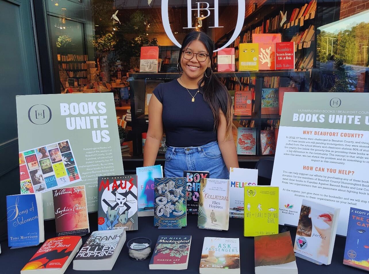 Julia Romero, a social media intern and student at Boston College, stands in front of a table full of books for sale. Hummingbird Books has sold and shipped many banned books to Families Against Books Bans and Lowcountry Pride, organizations that help provide students in Beaufort County with otherwise inaccessible books. Photo courtesy Hummingbird Books.