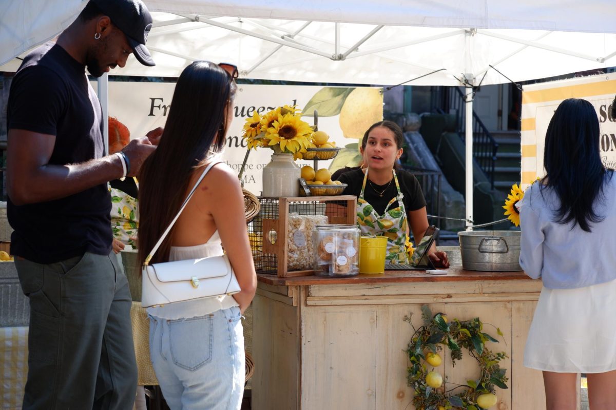 A woman sells freshly squeezed lemonade at her tent. The lemonade attracted a large line of customers wanting a break from the heat of the open street.