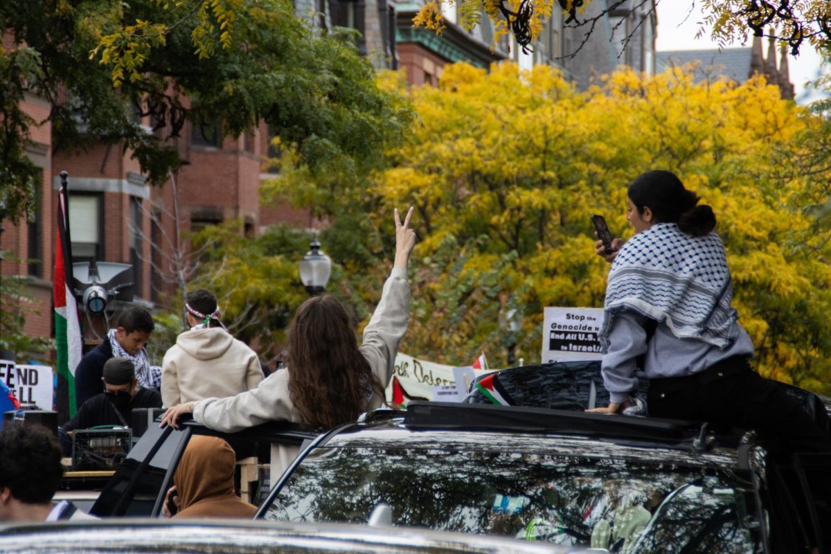 An activist makes the peace sign to the passing crowd while another activist films the scene. Protestors and members of the media recorded the march from all angles as it proceeded toward the Israeli Consulate.