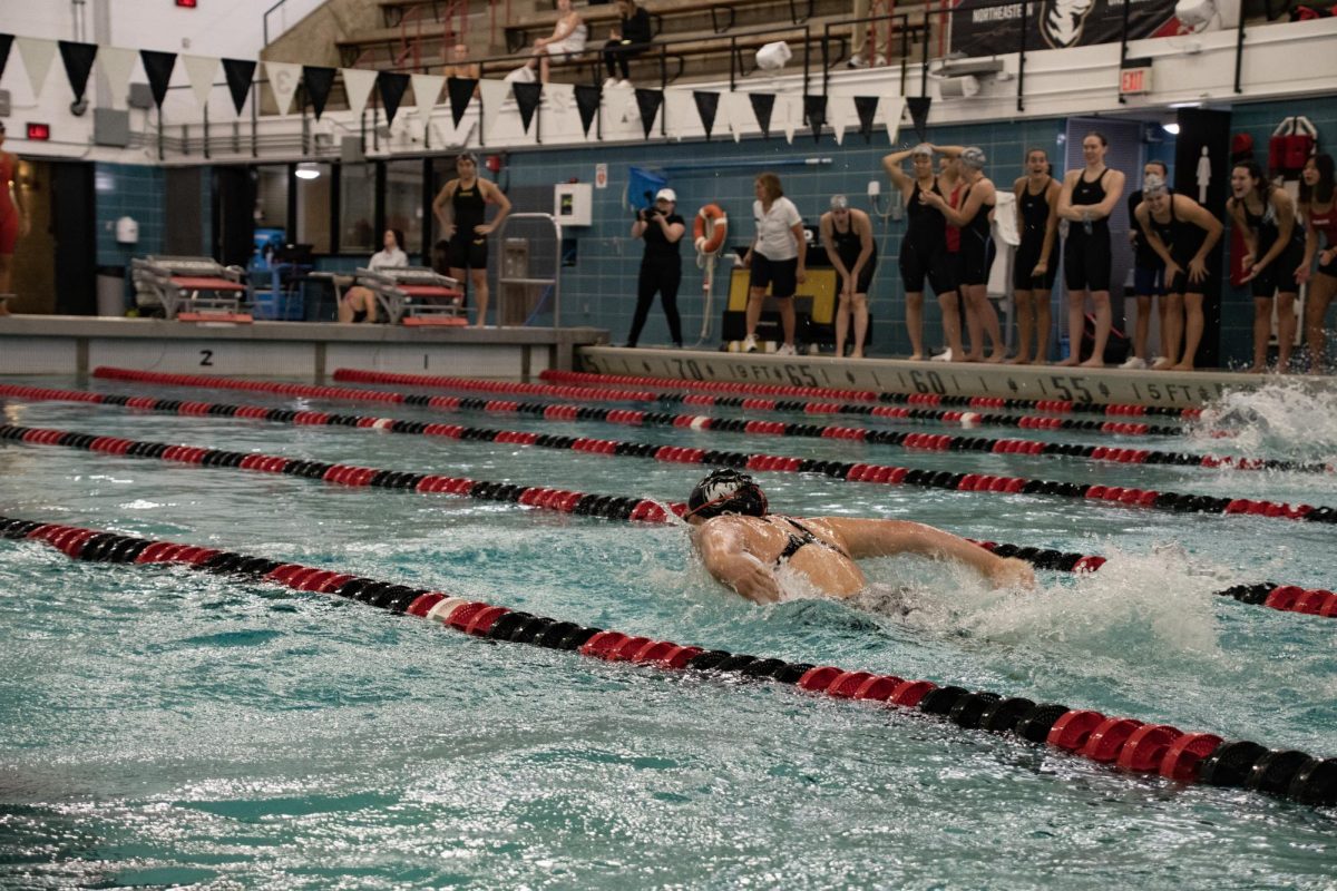 Daphne Peterson, a junior freestyle swimmer, competes in the 100-yard butterfly while the red team cheers from the sidelines. Peterson was placed on the CAA Commissioners Honor Roll for Fall 2022. 