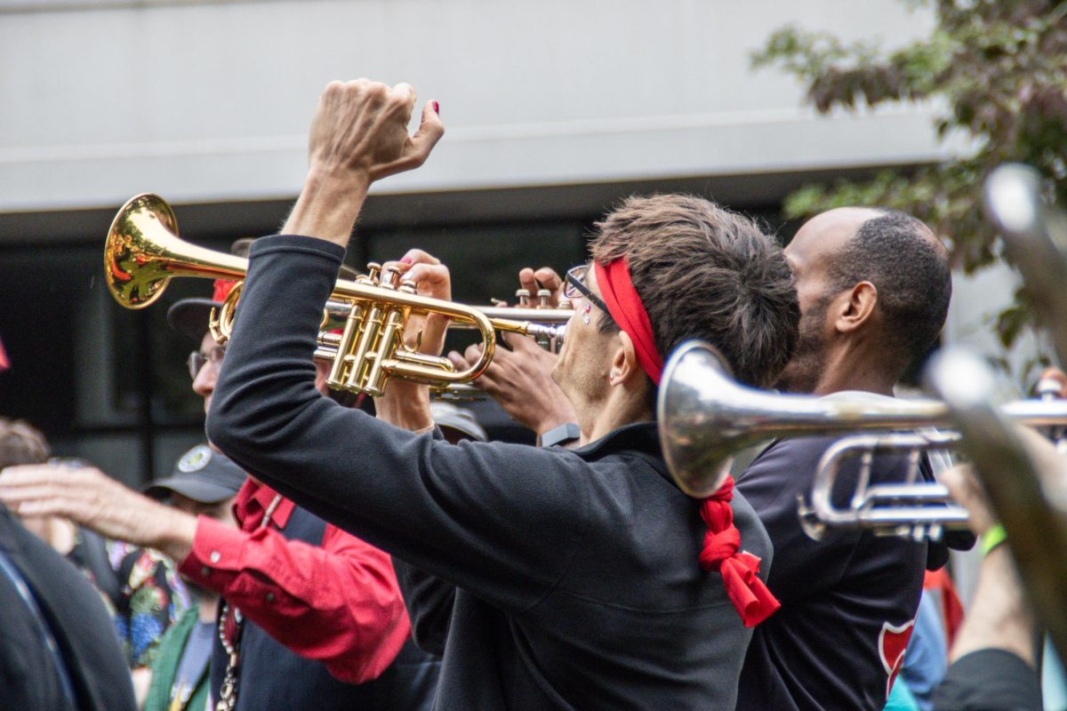 A trumpet player raises a fist mid-song in Davis Square Park. Many street bands at HONK! Festival engaged in local social justice activism alongside their performances.