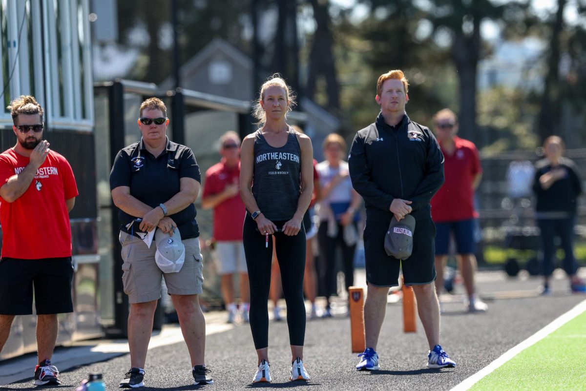 Northeastern field hockey coaches Pam Spuehler (center), Colin Clarke (right) and Cheri Schulz stand on the sidelines at Dedham Field. The Huskies saw a complete turnover of coaching staff during the 2023 offseason.