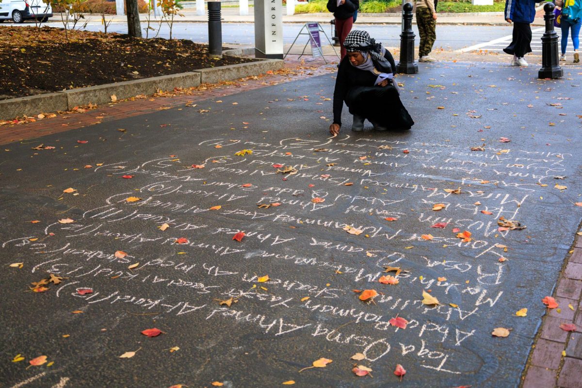 A student writes down names in chalk on the sidewalk in Centennial Common. Around 20 to 30 participants helped write the names of casualties.