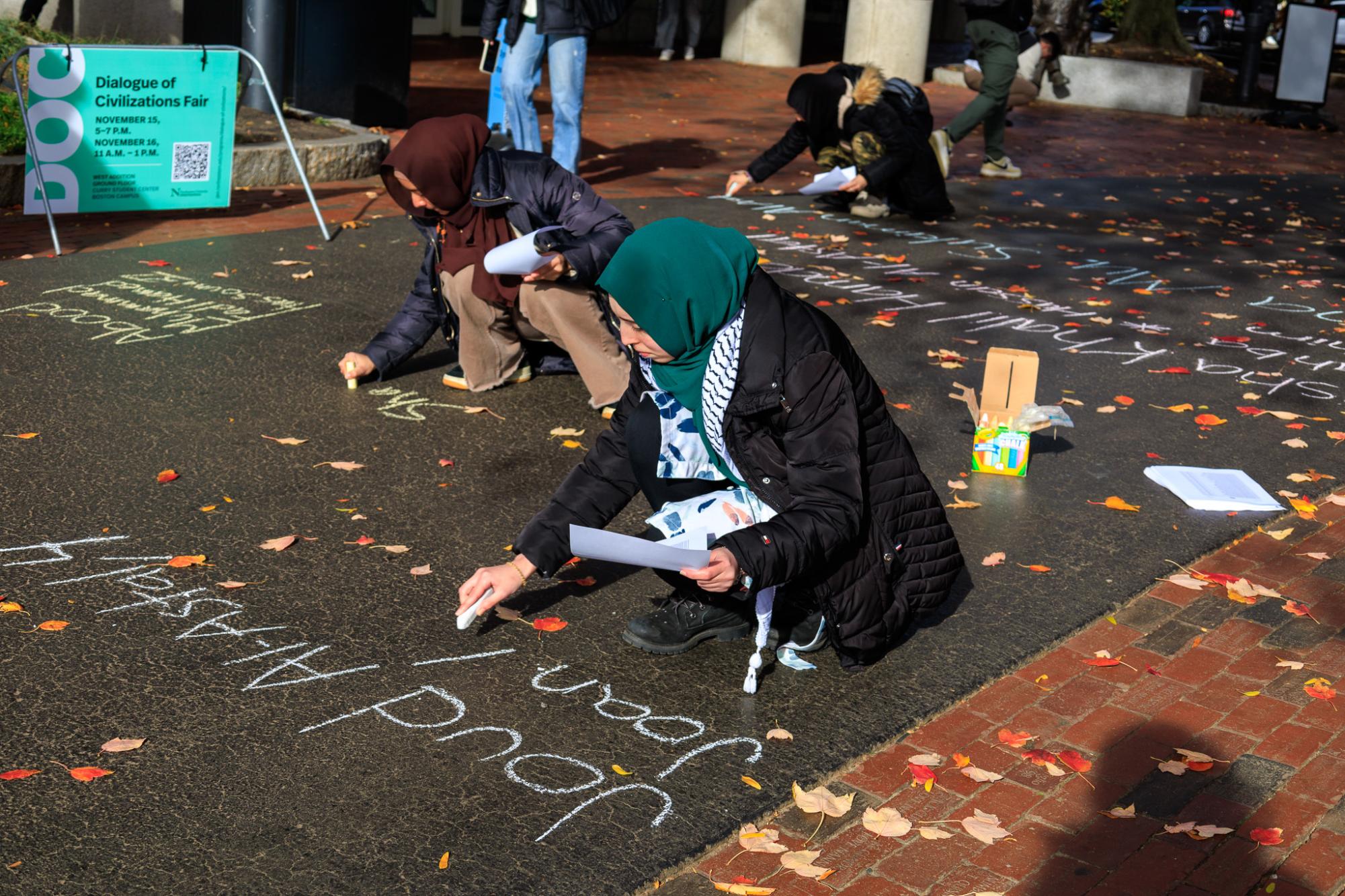  A participant in the chalk-in references the list of  Palestinians killed in Israels counterattack,  as she writes in chalk on the sidewalk. The list of names was also posted in the window of the Northeastern School of Law. 