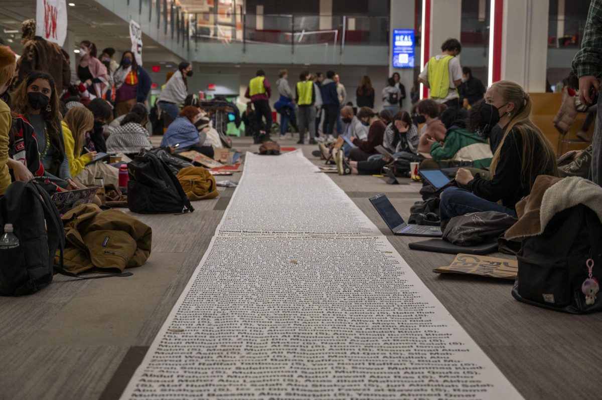 Students+gather+around+a+white+scroll+enumerating+the+names+of+hundreds+of+Palestinian+children+killed+in+the+Israel-Hamas+war+at+a+Dec.+1+sit-in+in+Curry+Student+Center.+The+demonstration%2C+organized+by+HFP%2C+resulted+in+some+participants+facing+disciplinary+action+from+the+university.++