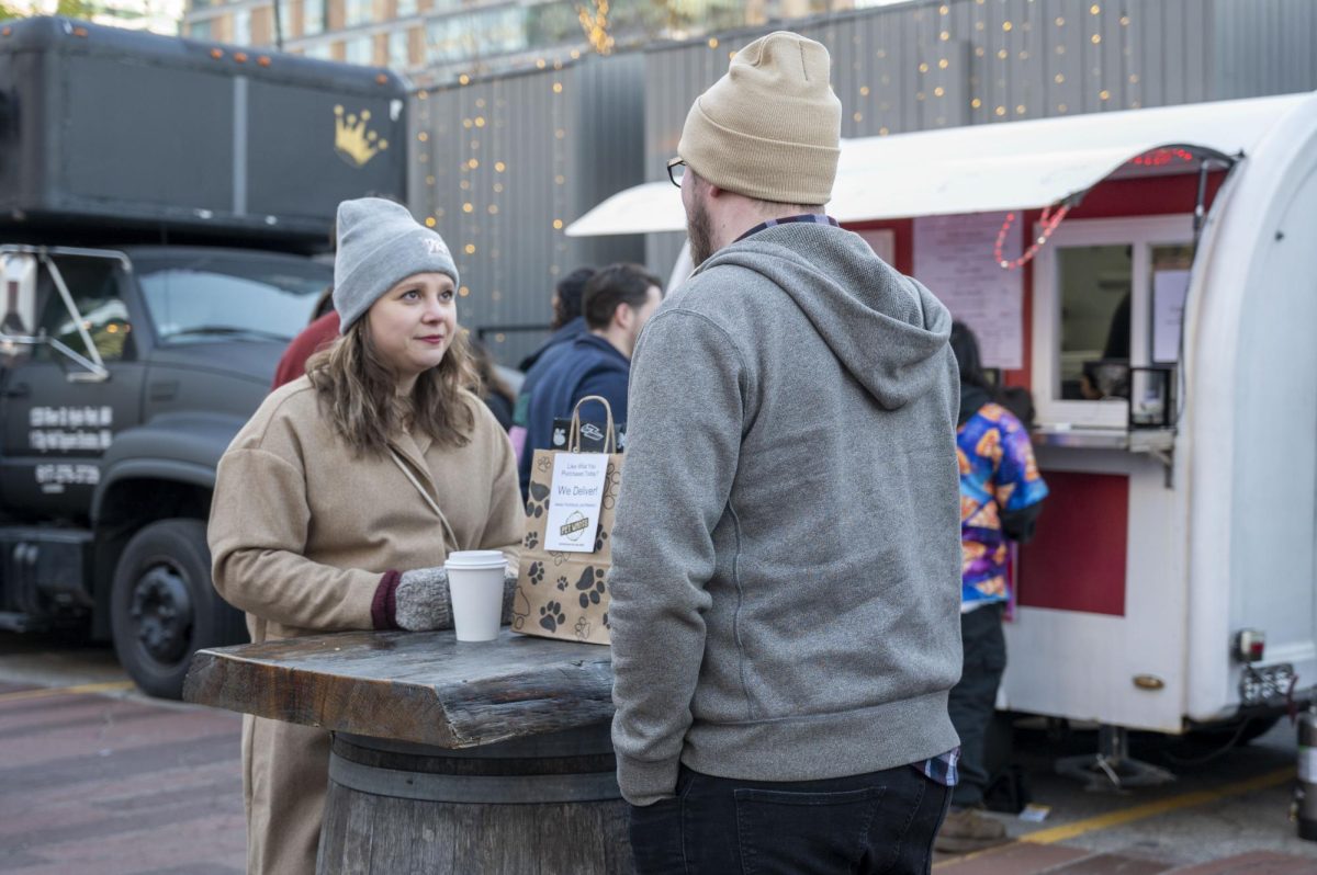 Two shoppers enjoy a hot drink while chatting at a standing table. The market offered many opportunities to catch up with friends and family.