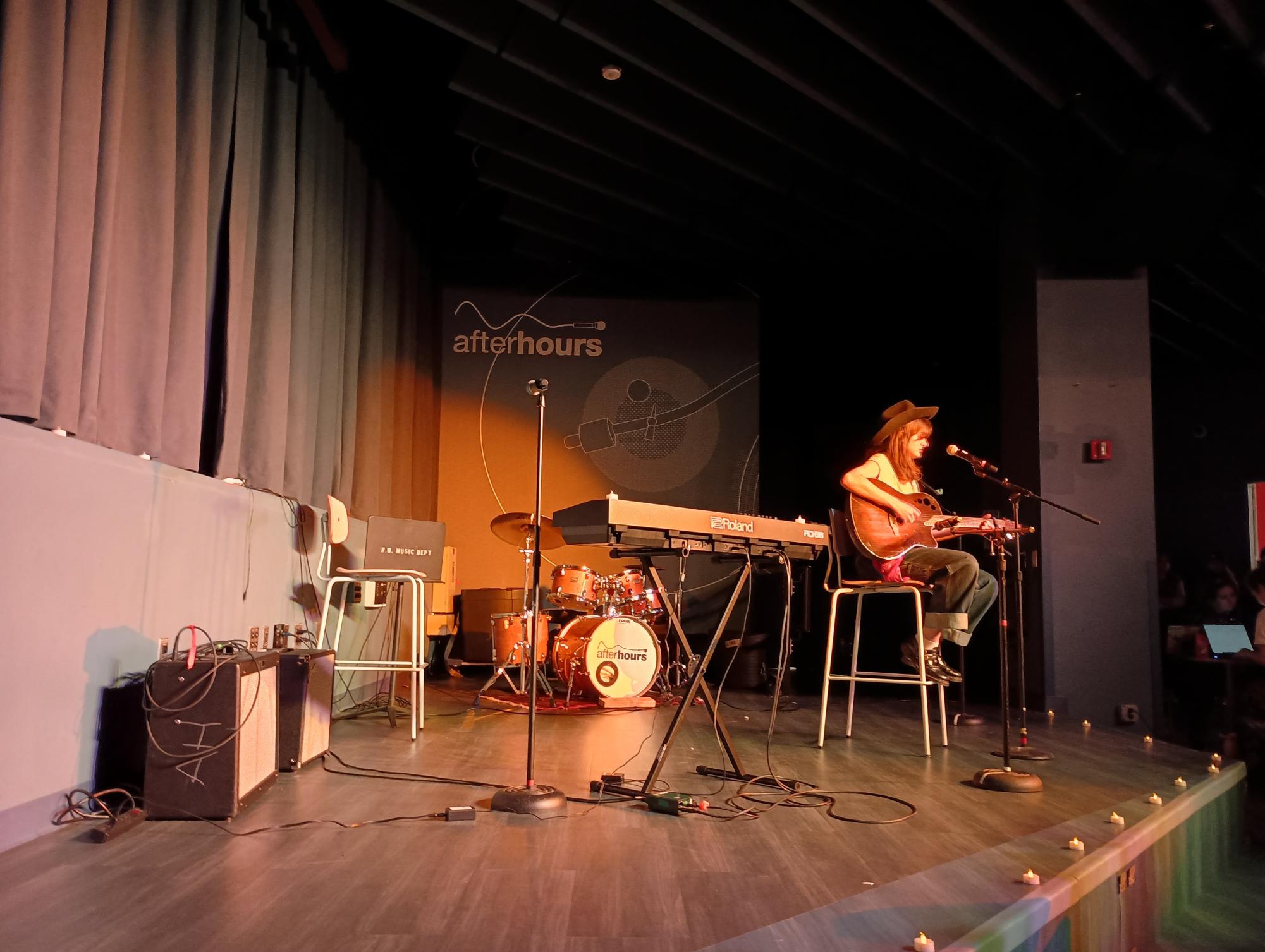 A performer strums their guitar and sings onstage. The proceeds from the open mic supported the Okra Project, a mutual aid organization for queer people of color.