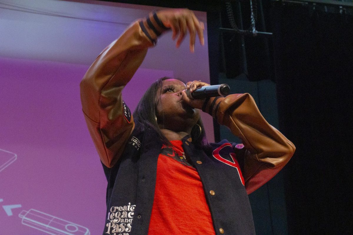 Ché Noir sings into a mic while motioning her hand at the audience. All artists at the event performed music featuring themes of the struggles of social structures and the power of passion.