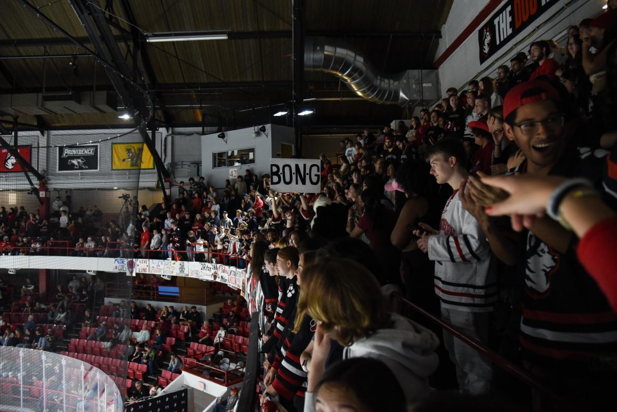 A student fan in the DogHouse holds up a sign that reads “B.O.N.G.” during a Northeastern power play. The DogHouse crafted signs like these to engage the section, with fans following the play by spelling out words one letter at a time and finishing with a phrase, in this case “Light the Lamp.”