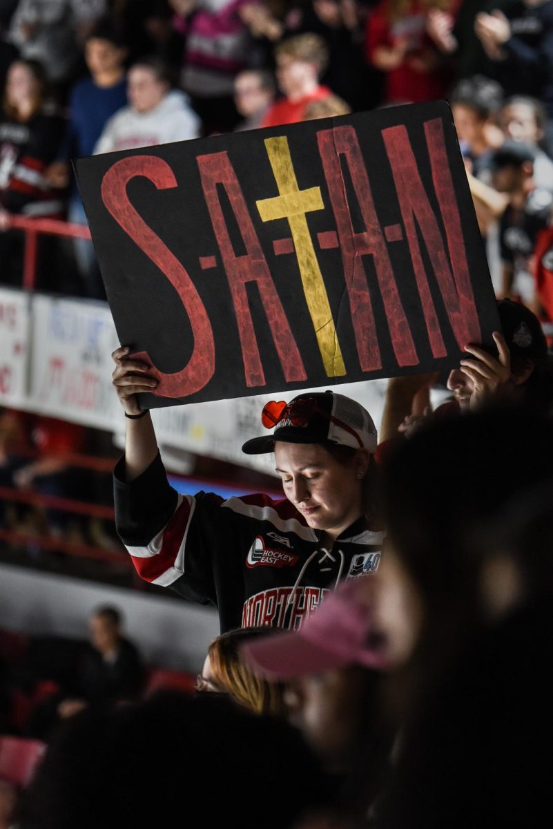 A student in the DogHouse holds a sign that reads “S-A-t-A-N” during a Northeastern power play. Like the “B.O.N.G.” sign, this increased the energy in the section.