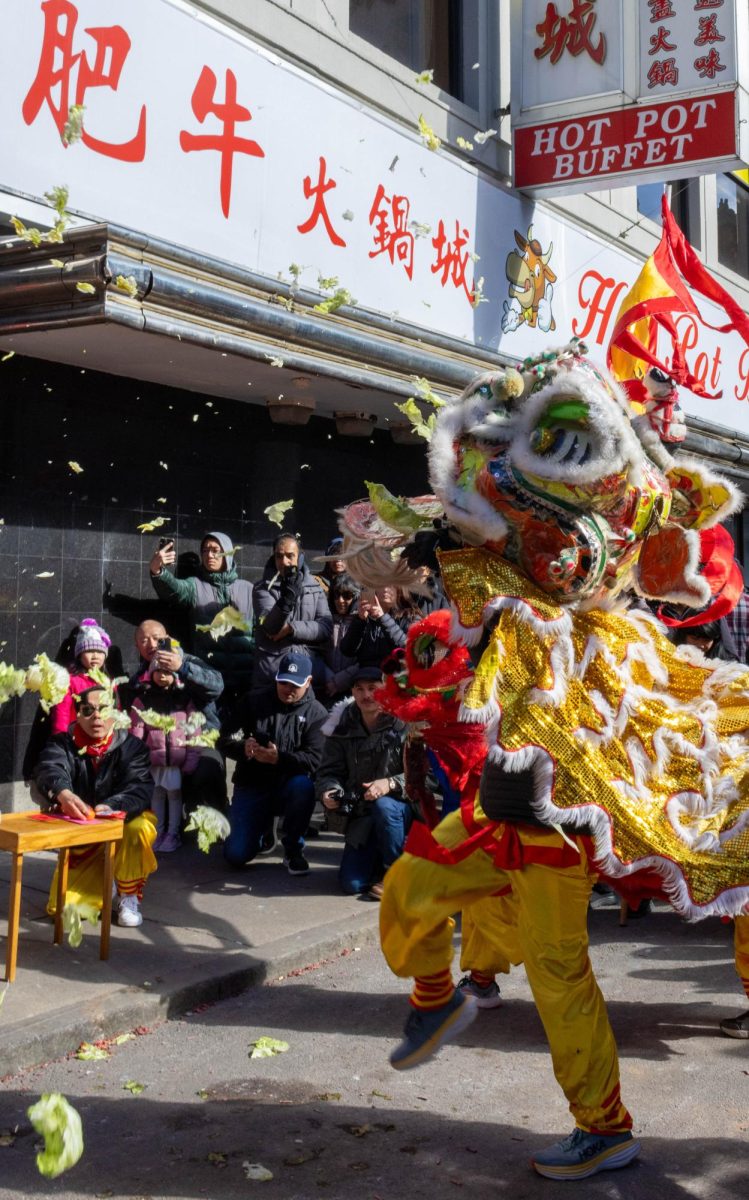 A lion dancer tosses lettuce into the air after receiving it from Hot Pot Buffet, garnering cheers from the watching crowd. Lion dancers consumed and spat lettuce at the audience to spread prosperity, since the word “‘lettuce”’ in Chinese sounds similar to the word “wealth.”