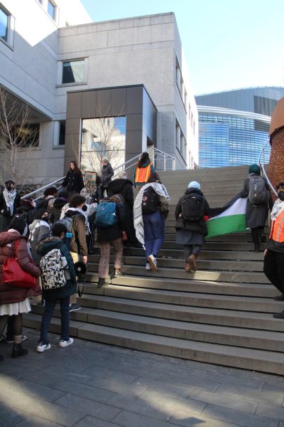 Students marching with HFP walk up the ISEC Pedestrian Bridge stairs while holding a Palestinian flag. HFP organized a walkout Feb. 8 that started in Snell Quad and progressed to EXP, where students attempted to deliver a letter to President Joseph E. Aoun.