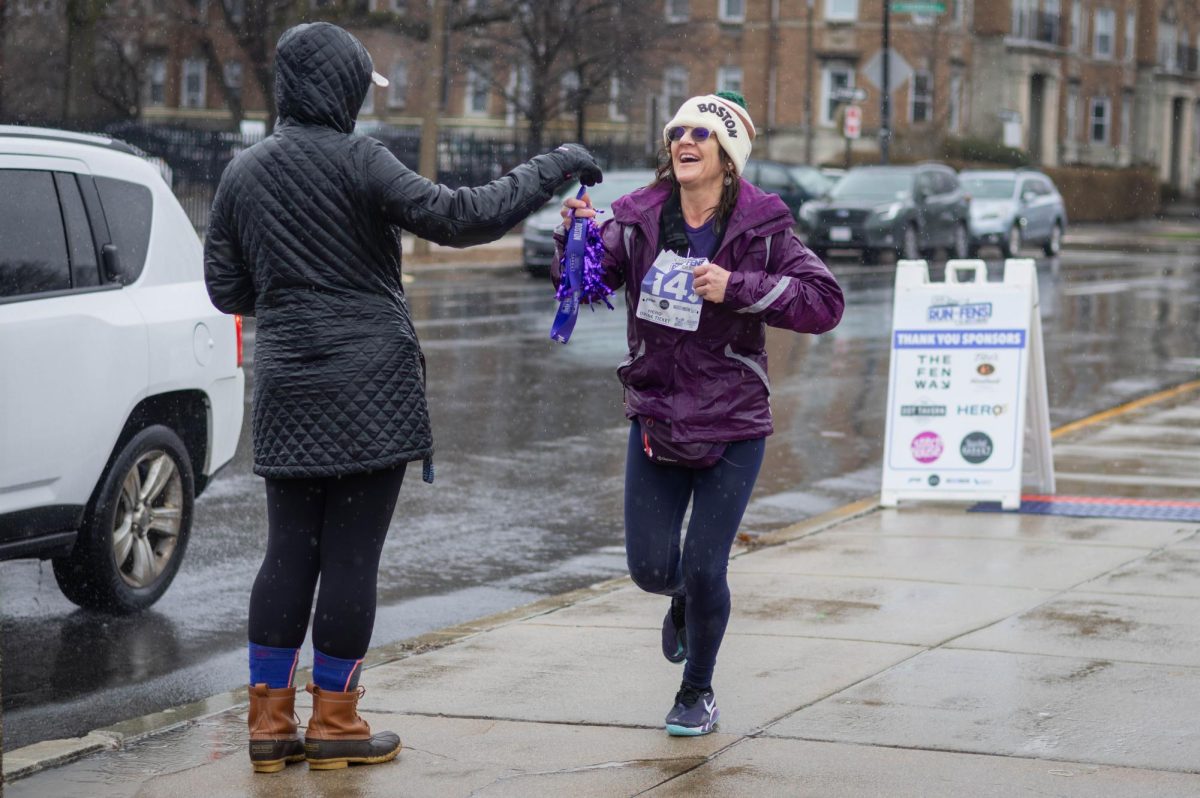 A participant crosses the finish line at the corner of Brookline Avenue and Park Drive  and collects their commemorative race medal. A booth set directly after the finish line played music and offered water bottles to runners.