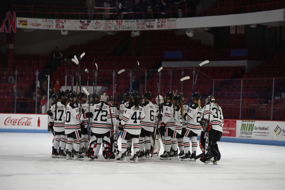 The Northeastern womens hockey team huddles at center ice. The Huskies skated to a 25-11-3 record on the 2023-24 season and finished second in Hockey East. 