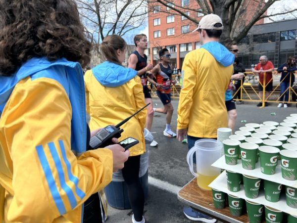 Maggie Heaney holds a radio as runners in the Boston Marathon pass by. The radio allowed Heaney to communicate across 23 channels with repeaters all over Boston.