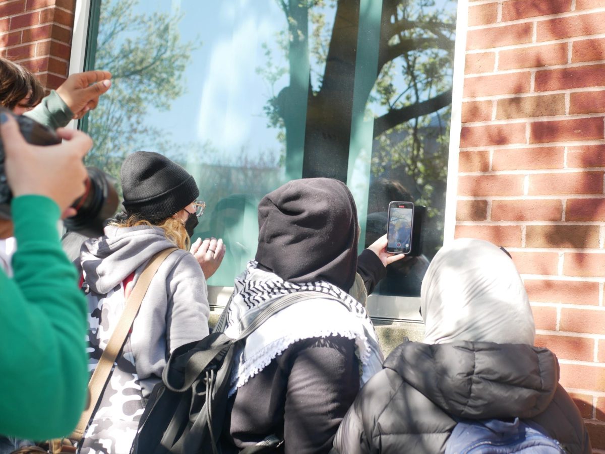 Onlookers look at detained protesters through the windows of Shillman Hall. The protesters inside appeared to shout identifying information at onlookers.