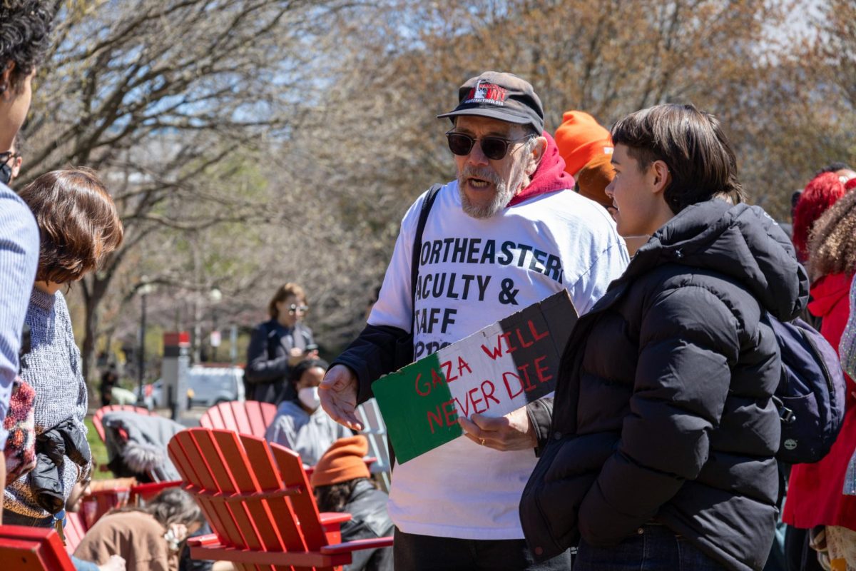 Marty Blatt, a professor of history and member of Northeastern Faculty and Staff for Justice in Palestine, speaks with a student about the ongoing encampment. He holds a sign that states Gaza Will Never Die.