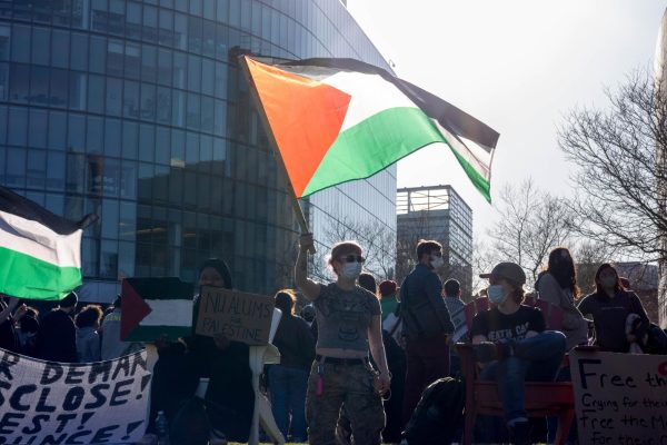A protester waves a Palestinian flag while other protestors hold up handmade signs. Prior to the sunset around 5:45 p.m. organizers hosted a meeting to discuss encampment plans overnight.