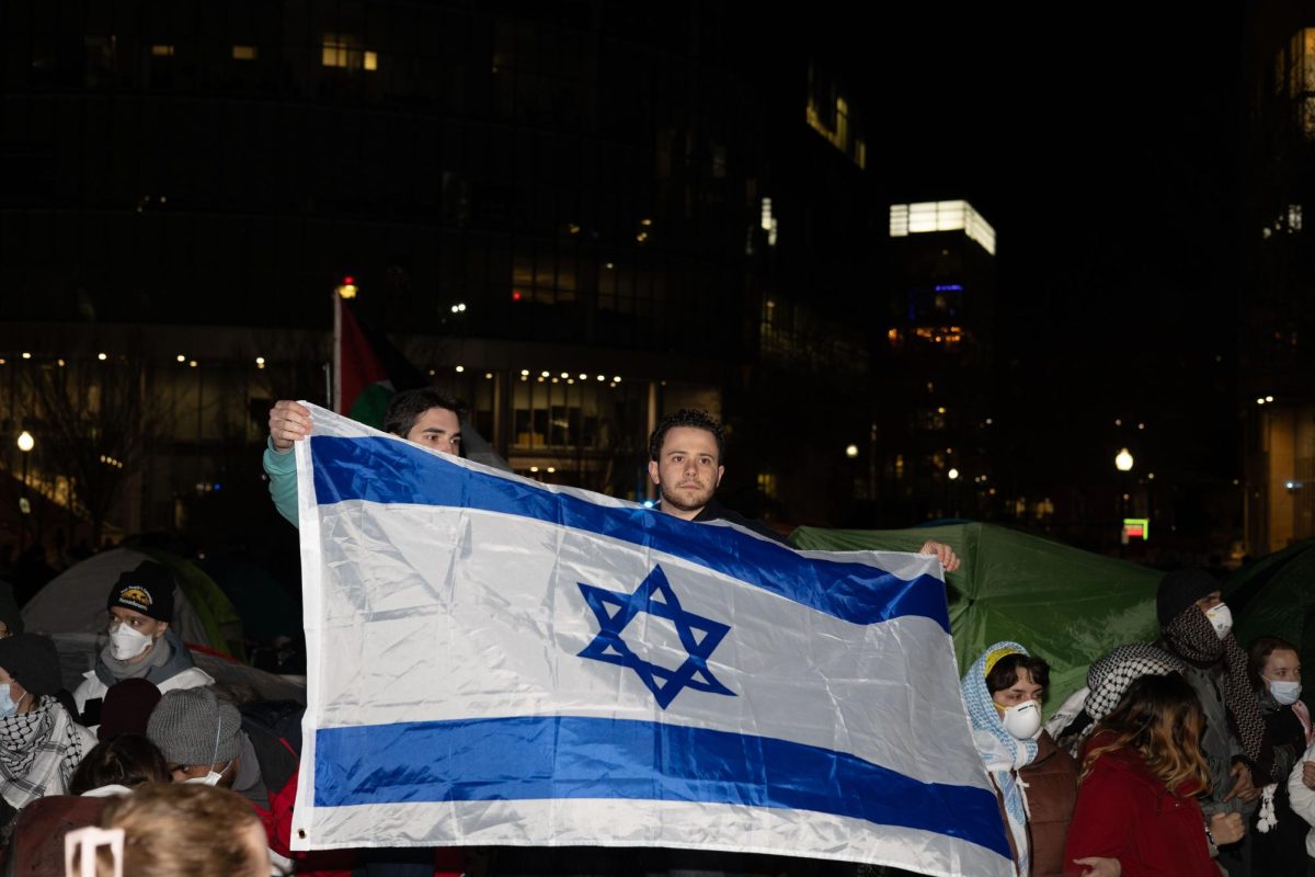 Two pro-Israel counter protesters hold up an Israeli flag in front of a crowd of pro-Palestine protesters Friday night. The Boston Globe updated their reporting on the Kill the Jews remark heard Friday night after video footage released Saturday revealed the remark was said by one of the pro-Israel protesters.