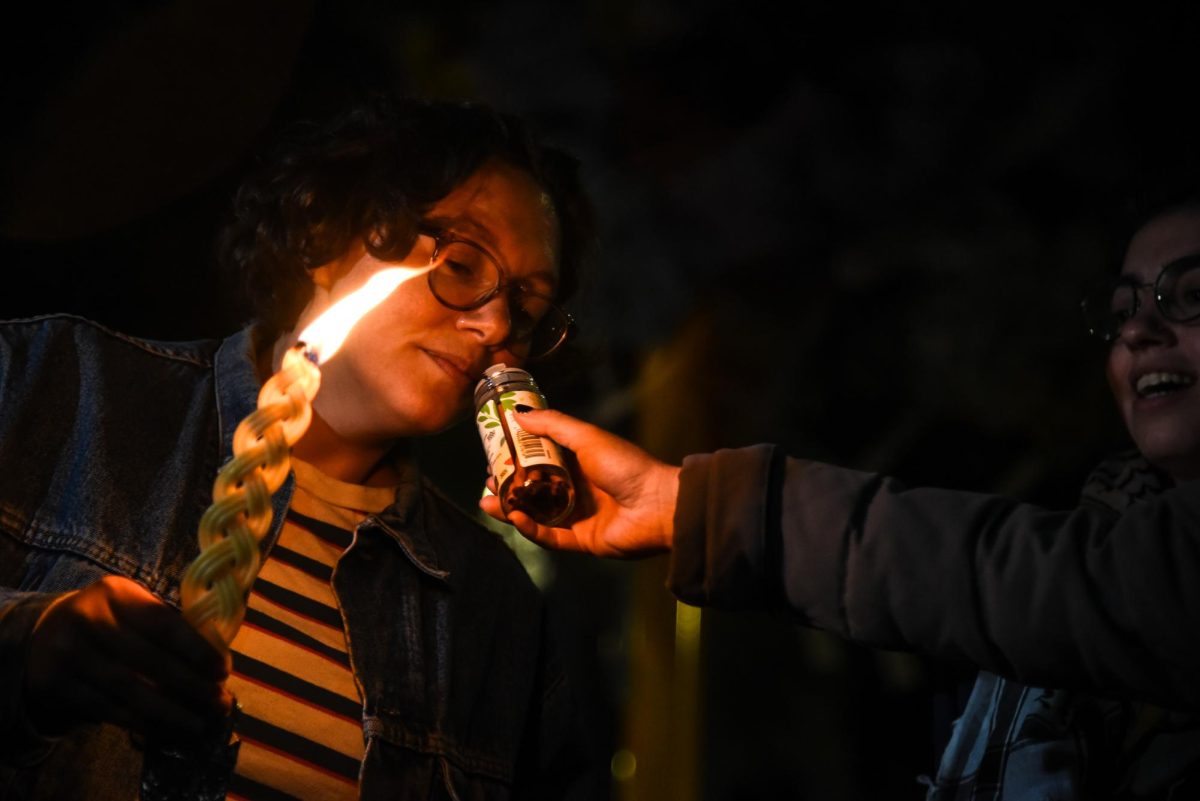 A Havdalah attendee sniffs spices while holding a lit candle.