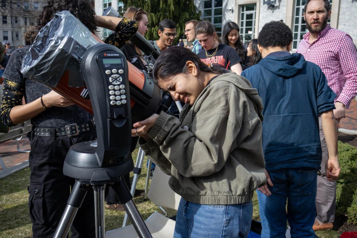 A student gazes through a Celestron Nexstar telescope, examining the moon as it overshadows the sun and creates a crescent shape. The Northeastern Mars Rover Team and SEDS brought at least three different types of telescopes to Krentzman Quad.
