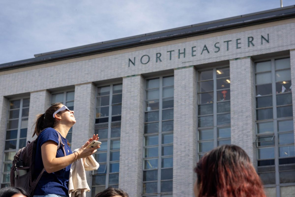 A student looks in awe at the eclipse, pulling out her phone for a picture. Students gathered to watch in many Northeastern spaces, such as Carter Field, Centennial Common and the Curry Student Center terrace.