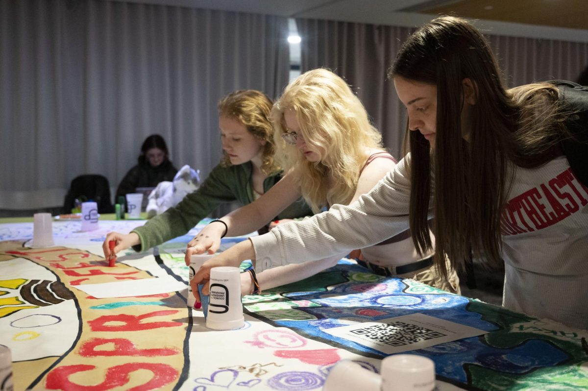 Three students contribute to the Springfest mural. Attendees were encouraged to make “Olympic rings” by tracing plastic cups.