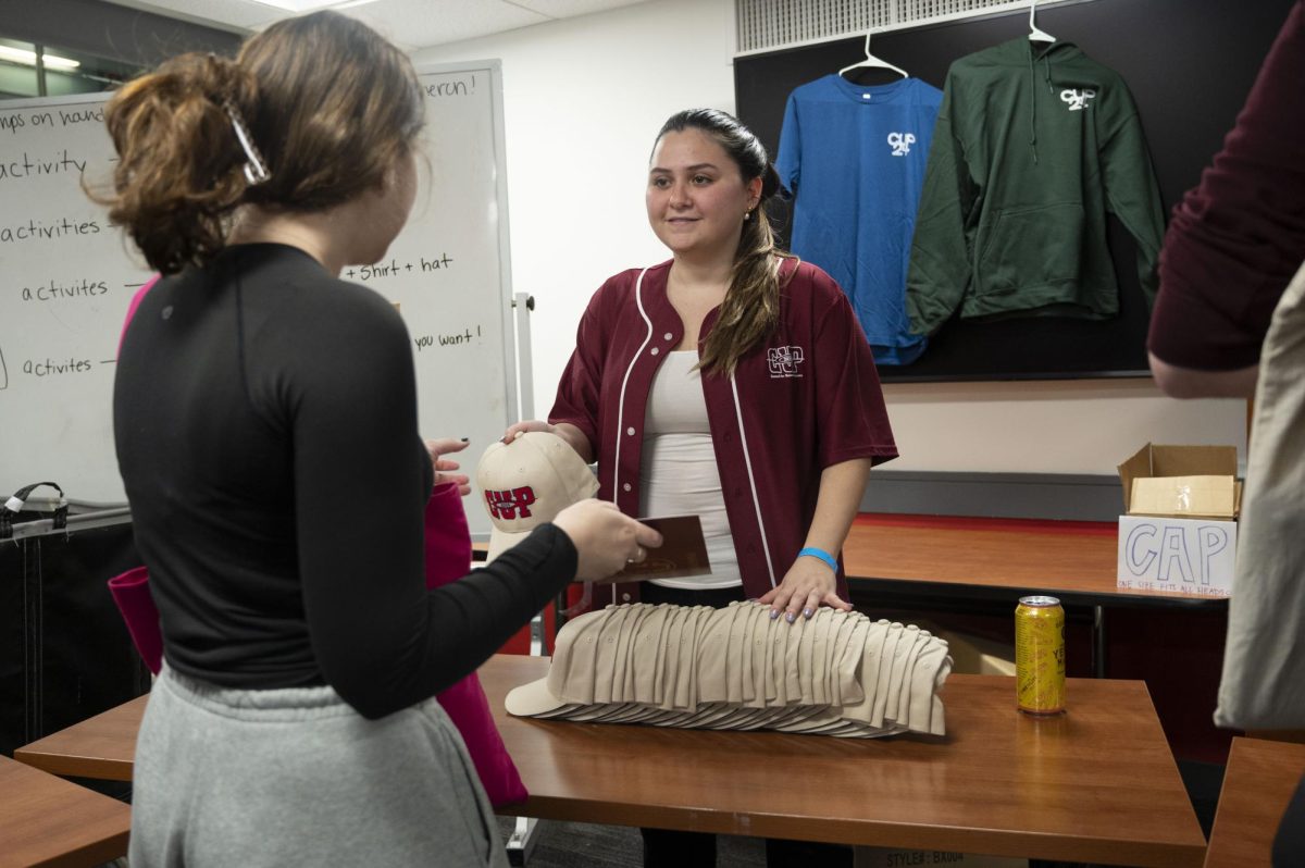 Rachel Moskowitz, a third-year business administration and communication studies combined major and CUP’s associate director of concerts, hands a student a CUP hat. The Springfest merchandise was broken into tiers based on the number of stamps students had, with each tier unlocking a different item.
