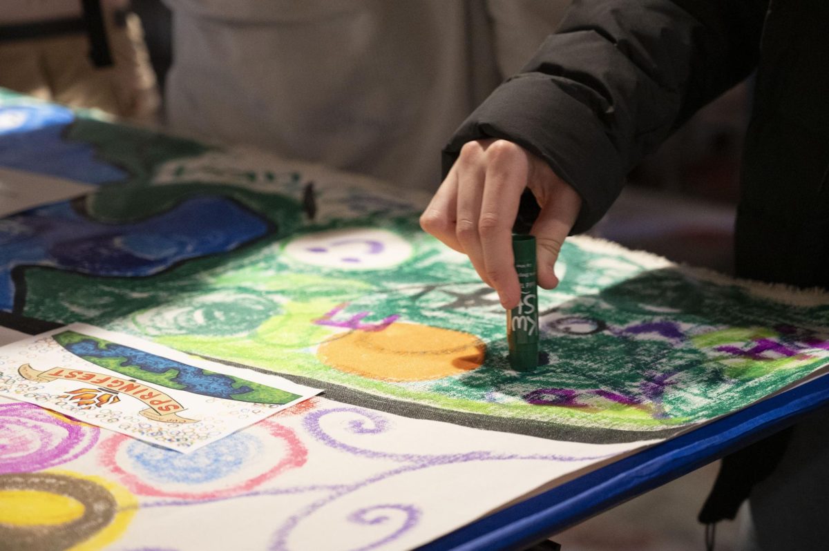 A student draws with a paint stick on the community mural. Tempera paint sticks were chosen as the mural’s medium for easier and cleaner use.