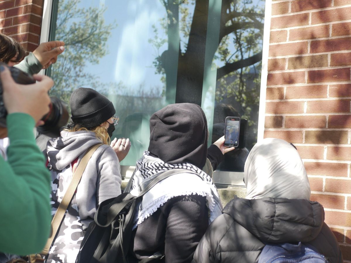 Onlookers look at and photograph detained protesters through the windows of Shillman Hall. The protesters inside appeared to shout their identifying information to the onlookers outside.