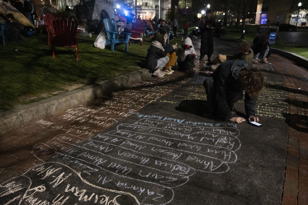 A protester writes the names of Palestinians killed by the Israeli military in chalk on the sidewalk surrounding the Common. HFP called for students to sign up for night shifts to guard the encampment while others slept.