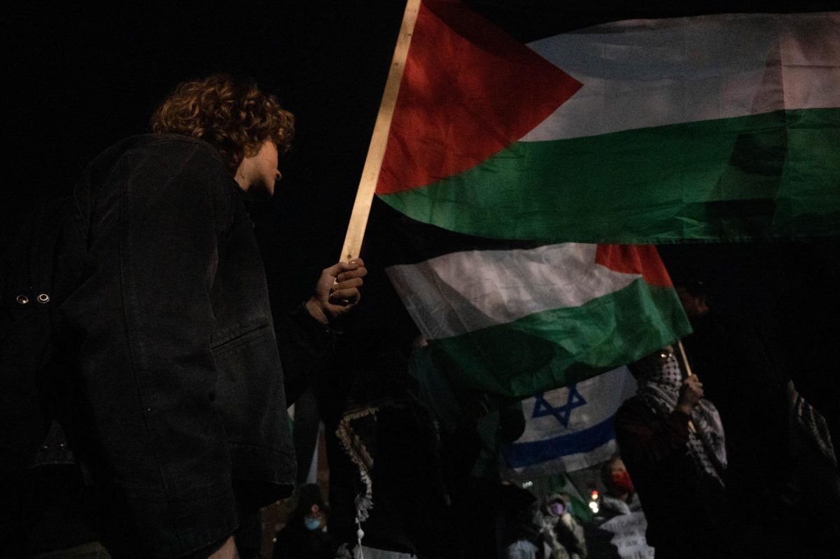 A pro-Palestine protester holds up a Palestinian flag in front of an identical flag and, behind it, an Israeli flag. As tensions rose, more pro-Palestine protesters attempted to cover up the Israeli flag with Palestinian flags.